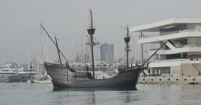 Ferdinand Magellan Nao Victoria carrack boat replica with spanish flag being docked in Valencia with veles e vents in the background in slow motion 60fps