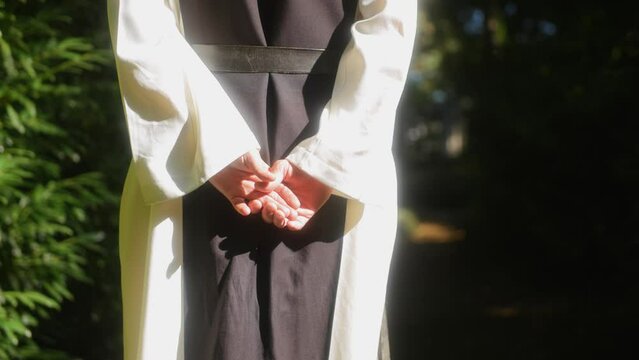 Close up shot of the hands of a monk walking in the forest towards the light