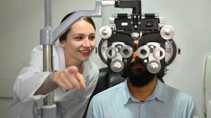 Female doctor ophthalmologist is checking eye vision of Indian man in modern clinic