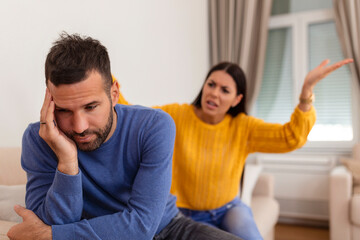 Fototapeta premium Young couple having argument - conflict, bad relationships. Angry fury woman. Angry young couple sit on couch in living room having family fight or quarrel suffer from misunderstanding