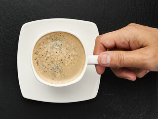 Hand is giving a cup of coffee on a black background. Espreesso
