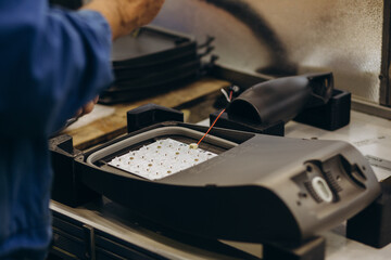 Hands of african man with electric screwdriver, working with electric sceme for LED lamps. He is sitting at his working table, wearing uniform