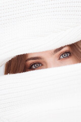 Beautiful girls blue eyes between two sleeves of white woolen sweater, creative portrait. 