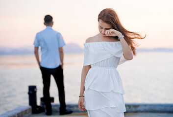 Young couple break up at the sea deck. Girl crying and walk away from man in concept love hurts...