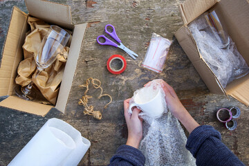A woman packs a glass cup in a plastic bubble wrap. Fragile package.