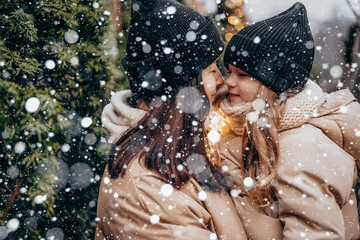 Obraz premium Winter holidays and people concept - happy morther and little daughter choosing christmas tree at street market. Happy family buys a Xmas tree.