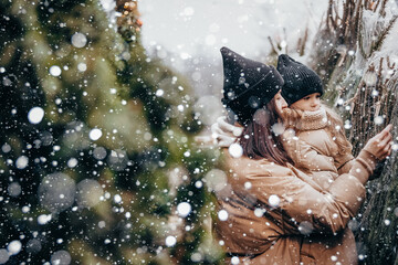 Winter holidays and people concept - happy morther and little daughter choosing christmas tree at street market. Happy family buys a Xmas tree.