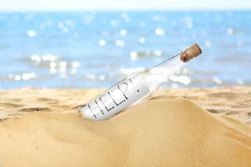 Corked glass bottle with rolled paper note on sandy beach near ocean