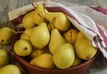 Ripe yellow pears in clay bowl on wooden table indoors. Traditional dishtowel on background. Season...