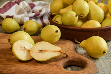 Closeup sliced pear pieces on wooden cutting board. Ripe yellowish pears in clay bowl on wooden...