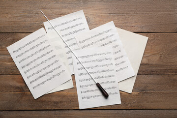 Conductor's baton and sheet music on wooden table, flat lay