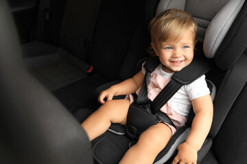 Cute little girl sitting in child safety seat inside car