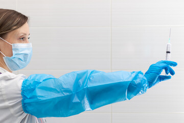 Young woman doctor in a medical mask and gloves with a syringe in her hand and a stethoscope in a...