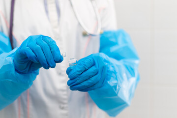 Doctor's hands in rubber medical gloves hold an ampoule of medicine in a hospital during the coronavirus pandemic. Selective focus. Close-up