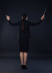 Professional conductor with baton on dark background, back view