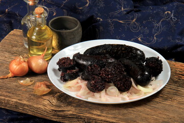 Baked black pudding with pickled onions on a white plate. Sliced and fried blood sausage on a plate