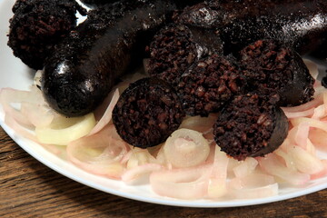 Baked black pudding with pickled onions on a white plate. Sliced and fried blood sausage on a plate