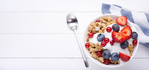Crunchy granola with yogurt, muesli and berries on white wooden background, top view, space for text.