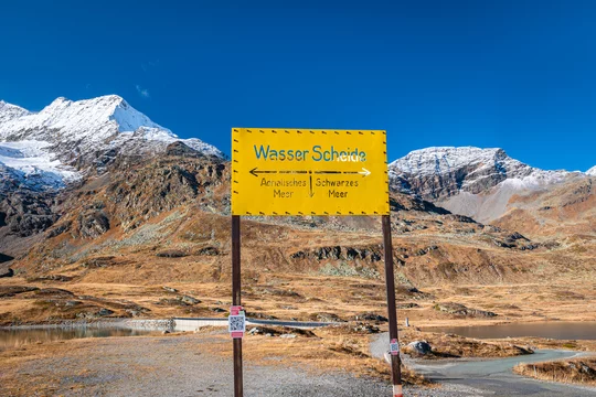 Sign on Bernina Pass, Switzerland, indicating a watershed in the Alps,  where on the left the water flows to the Adriatic Sea and on the right to  the Black Sea. Stock Photo