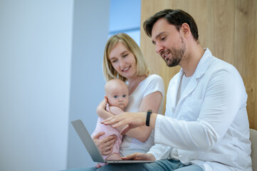 Blonde young woman with a baby talking to a pediatrician in the clinic