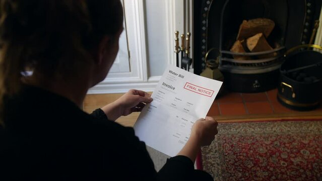 An unrecognizable female opening a debt letter. The woman is reading a water bill notice at home