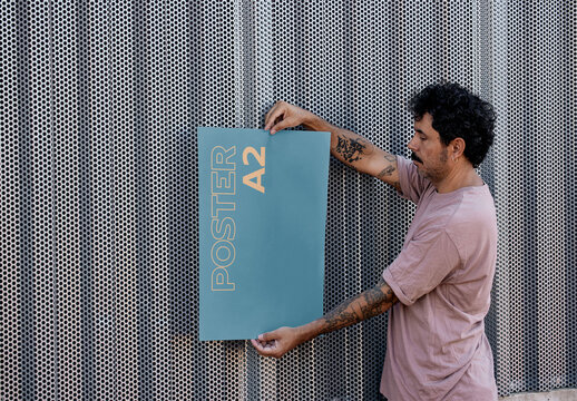 Man Holding a Vertical Poster Mockup on a Wall