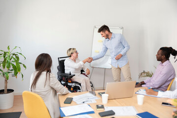 businesswoman in the wheelchair with a disability shakes coworker's hand at business meeting
