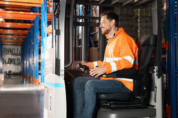 Happy worker sitting in forklift truck at warehouse