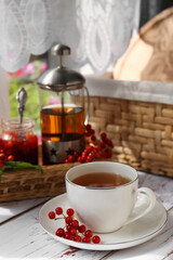 Cup of hot drink and viburnum berries on white wooden table indoors