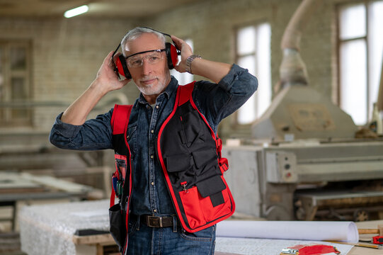 Mature Man In Eyeglasses And Ear Protector In A Workshop