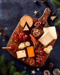 Christmas cheese platter with grapes, nuts, figs on a dark background. Top view. Xmas gourmet holiday appetizer. Copy space, top view.