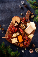 Christmas Cheese board appetizers platter with various types of cheese, crackers, jam, fruits, grape on a dark background. Overhead view, cope space.