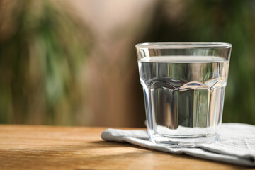 Glass of pure water on wooden table against blurred background, space for text