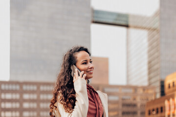 young elegant business woman talking on cell phone outside in downtown city at golden hour while...