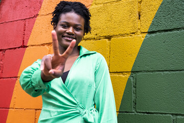 Smiling young woman gesturing peace sign in front of colorful wall
