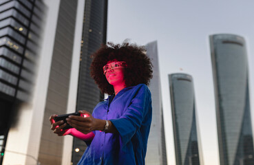 Red light falling on woman face wearing smart glasses holding smart phone in front of building
