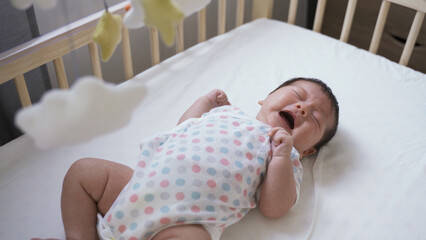 high angle shot upset newborn infant lying alone in the baby bed is crying and screaming loudly in...