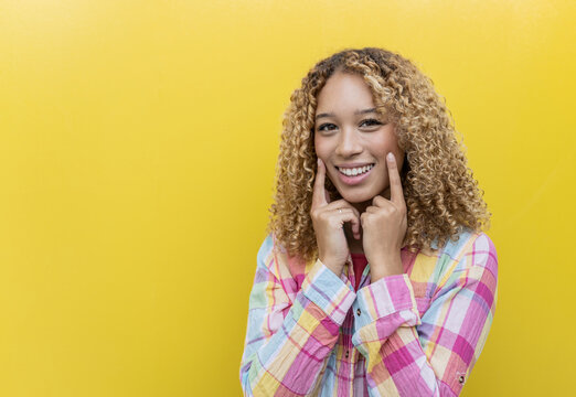 Smiling woman with fingers on cheeks over yellow background