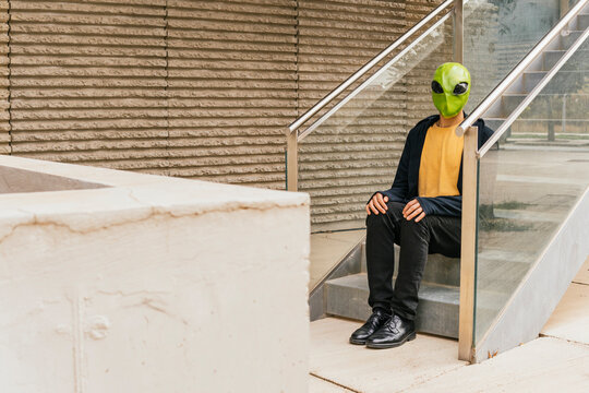 Man wearing alien mask sitting on staircase