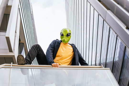 Man wearing alien mask jumping over railing in front of building