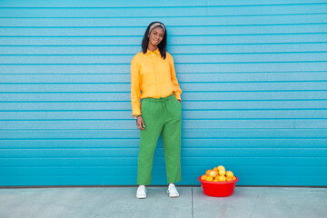 Young woman standing with basket full of oranges in front of blue wall