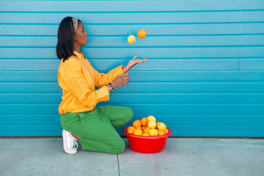 Young woman juggling with oranges in front of blue roller shutter