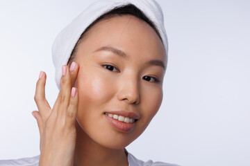 Closeup of asian woman with towel on head apply white cream on face. Young girlportrait. Neutral natural pink manicure on nails. Woman doing cosmetic procedure, white background, isolated.