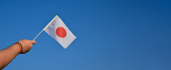 Japan flag and rainbow flag raising in hands which has rainbow wristband and against bluesky, soft and selective focus, concept for LGBT celebrations and events in pride month in Japan.