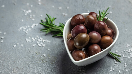 pink olives with fresh rosemary in a small bowl, on light wooden background. Long banner format. top view