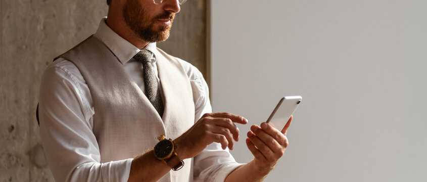 Banner crop of businessman in vest and shirt using mobile phone in modern office, banner 