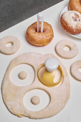 Cropped close-up shot of raw dough being cut into donuts with a doughnut mold, dipping tongs with a...