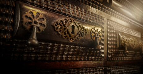 Fototapeta na wymiar Shallow focus against keyhole in ancient furniture locker with suggestive light effect. Secret drawer. 