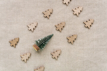 Fototapeta na wymiar Abstrakt von kleinen goldenen Weihnachtsbäumen und ein grüner Tannenbaum. Design, beiger Leinen HIntergrund.