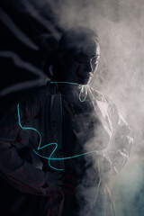 Young woman with glowing led band portrays bloodthirsty zombie against smoke background.